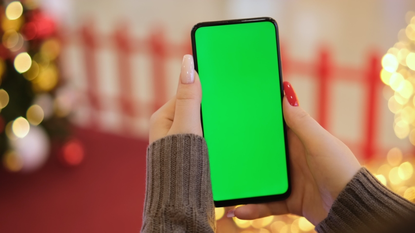 Hand of a young woman with a smartphone with a green screen on a red background with New Year