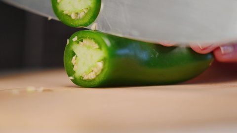 Chef's hand cutting green jalapeño pepper with sharp knife onto cutting board into pile of slices in slow motion