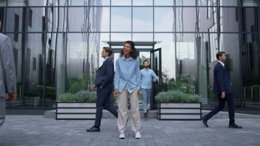 Successful corporate worker celebrating triumph laughing in urbanistic workplace. Attractive joyful lady screaming raising hands up in middle of crowd outside. Professional woman being happy at work. 