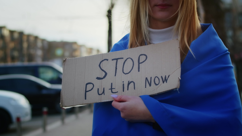 Portrait of a joyful Ukrainian woman holding a Ukrainian flag and a sign. The girl is waiting for her husband from the war. War between Russia and Ukraine.