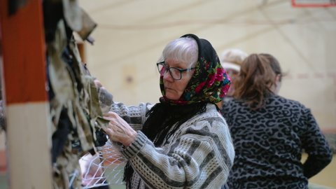 Ukraine, Chernivtsi - March 4, 2022: Grandmother and women weave camouflage nets for Ukrainian troops defending territory of Ukraine during war. Protective mesh helps to hide from enemies