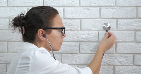 Doctor with stethoscope in ears. A view of a smart doctor with a stethoscope in her ears listen the wall in the room.