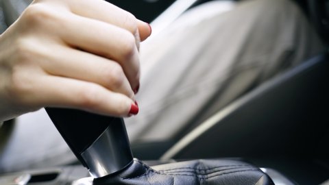 Close up of a white woman with red nails hand in casual clothes at the wheel of a car, shifting gears in auto. European girl drives an automobile.automobile, steering, driving, gear, drive, gearbox, s