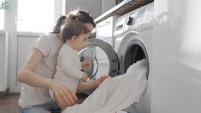 young mom take out clothes from washing machine with baby girl toddler in kitchen. in house. Family-housekeeping. mother using washing machine for wash - Powered by Shutterstock - Get 15% off with code: PIKWIZARD15