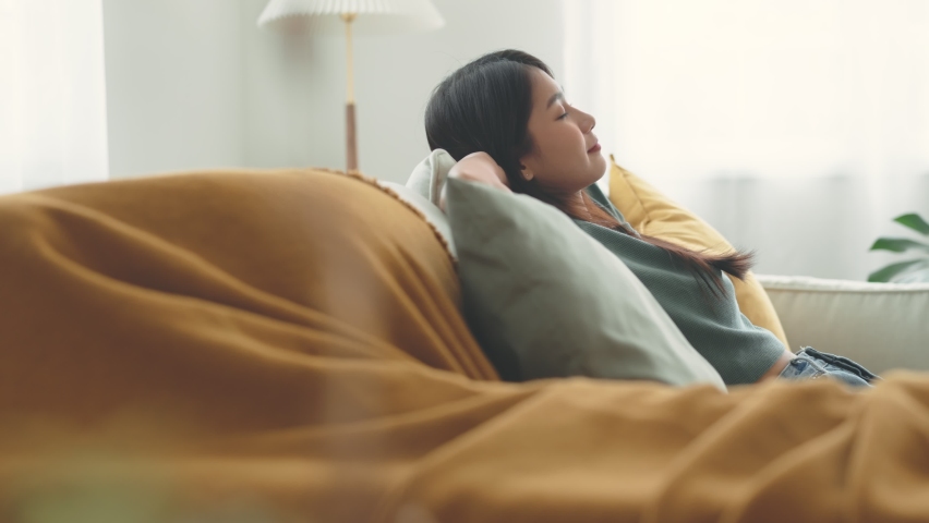 Relaxed young asian woman enjoying rest on comfortable sofa at home, calm attractive girl relaxing and breathing fresh air in home. Royalty-Free Stock Footage #1088782525