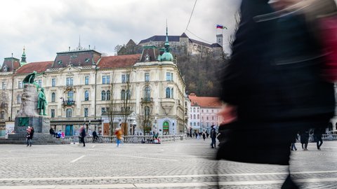 LJUBLJANA, SLOVENIA - MARCH 06, 2022: Time-lapse view on the people walking on the Preseren Square and the Tromostovje Triple bridge with the Ljubljana Castle in the background on a cloudy day