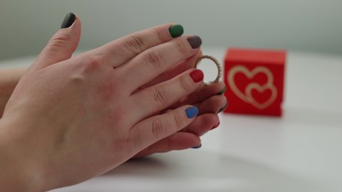 Close-up unrecognizable woman putting on engagement ring admiring jewelry at white background. Female hand with jewellery on finger with red gift box at background