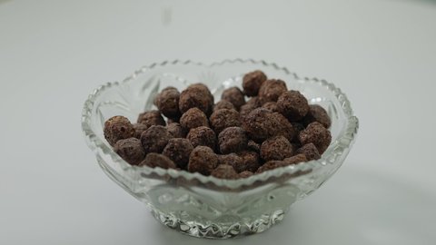 Milk pouring on chocolate cocoa balls in glass bowl. Dairy drink splashing on brown tasty sweet breakfast dessert indoors on table