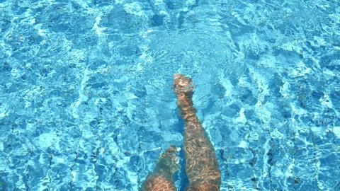 Slender beautiful long female legs in the pool swim and splash in the blue turquoise water. The concept of relaxation, summer vacation. Slow motion video. Summer time,  pool party. Copy space.