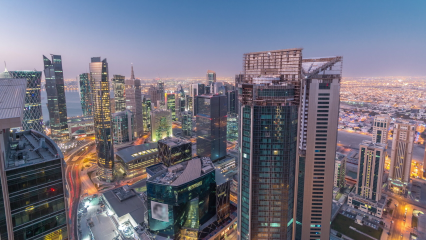 Skyline of the West Bay area from top in Doha night to day transition timelapse, Qatar. Illuminated modern skyscrapers aerial view from rooftop at morning before sunrise