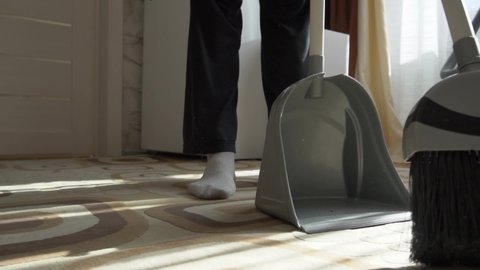 Sweep the dust from the floor with a brush. Dust rises into the air.  Sweep the dirt from the carpet in a dustpan. Clean the house. Do the cleaning. Close-up.  Cleaning service. Home cleaning routine.