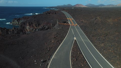 Aerial drone point of view volcanic rocky seaside and Atlantic Ocean of Lanzarote touristic Island, ruined washed out road leads to volcanoes. Canaries, Spain