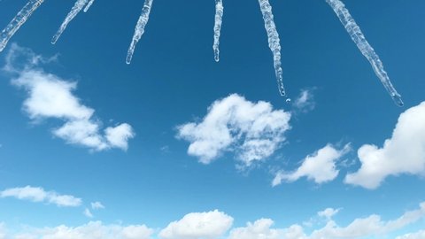 Few icicles melt in sun on spring day. Blue sky and white clouds. The first warm days after cold winter. Icicles glisten in the sun. 4K footage.