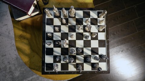 Ukraine, Chernivtsi - 11 February 2022: Chess board with black and white fields on which are placed metal chess pieces. Female hand makes move pawn. Top view. Chess game. Dark room. Retro atmosphere.
