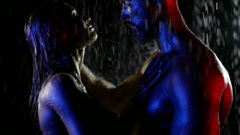 close-up of a couple with golden metallic skin. they stand in profile, closed eyes and touch each other at night in the rain. red, blue and white light. the dark key