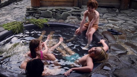happy family with kids relaxing in hot bath tub outdoors, enjoying thermal spa in stone vat on fire. winter activity and leisure