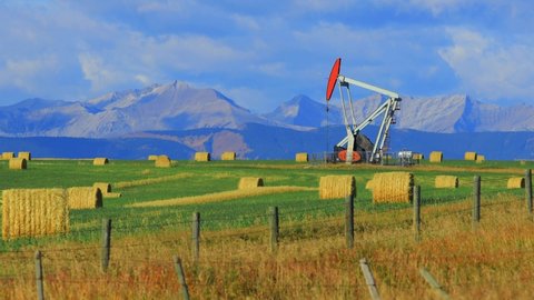 An oil and gas industry pumpjack drill rig in the Canadian Prairies with the Canadian Rockies in Alberta, Canada.