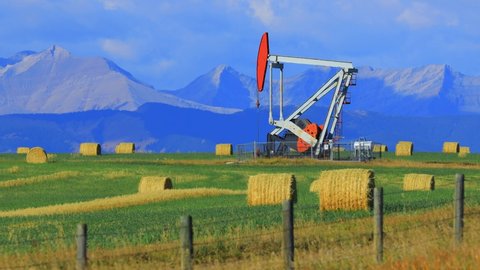 An oil and gas industry pumpjack drill rig in the Canadian Prairies with the Canadian Rockies in Alberta, Canada.