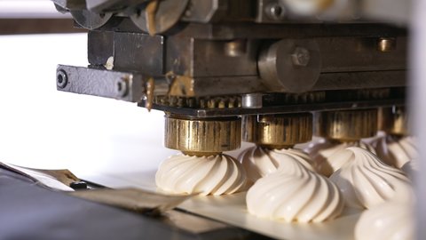 Few metal nozzles rotate and squeeze creamy marshmallows on conveyor belt. Automated line for desserts manufacturing. Close up.