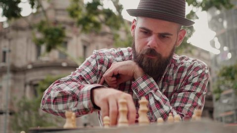 Spanish man playing chess outdoor. Latin bearded guy moving chess figures on a wooden checkered board. Strategy and thinking, brainstorming. 