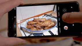 Female Hands Taking Photos of Prepared Juicy Roast Chicken on a Smartphone. Girl blogger shoots a picture, a photo review of food on a mobile phone camera. Photographing food. Home kitchen. Close up.