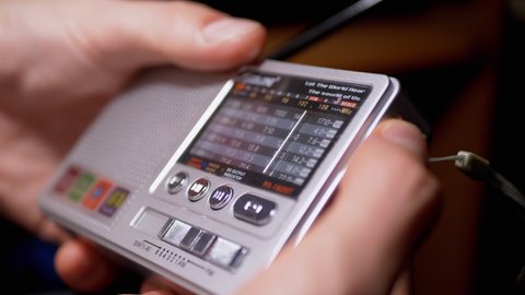 A Male Tunes a Radio Frequency on a Small Receiver with an Antenna. Hands hold an old radio in search of FM waves. Range setting. Searching for a station, rotation dial. A mini player with buttons.
