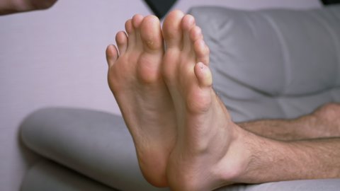 Female Hands Tickle Bare Male Feet, Toes, Outstretched on the Sofa. Person wiggles toes from tickling in a room. Reflex massage. Effective funny treatment improves blood circulation in soles. Zoom.