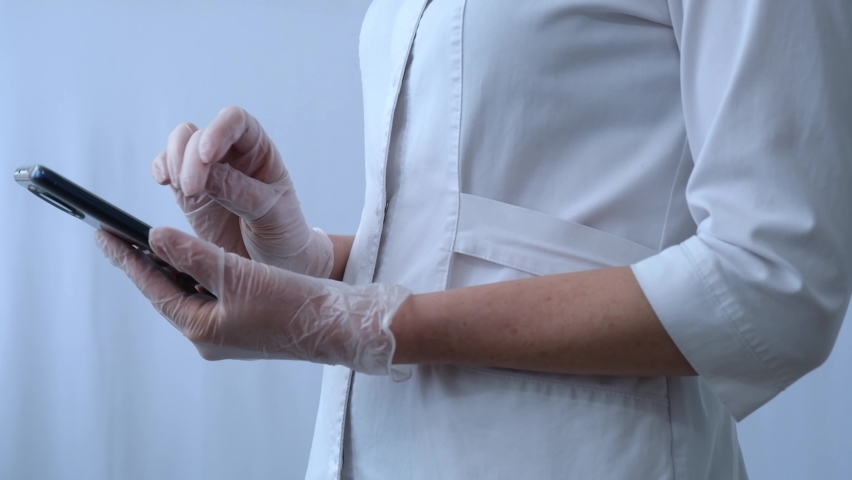 The doctor's hands are close-up. A female doctor on a cell phone is texting or looking for something. Scrolls through the social media page. Royalty-Free Stock Footage #1088803757