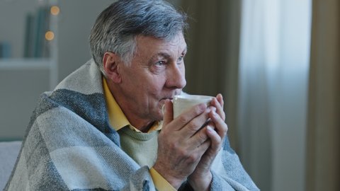 Close up portrait of pensive mature old man wrapped in warm blanket drinking hot tea calm grandfather resting alone enjoy delicious beverage relax happy dreamy elderly pensioner holding cup of coffee