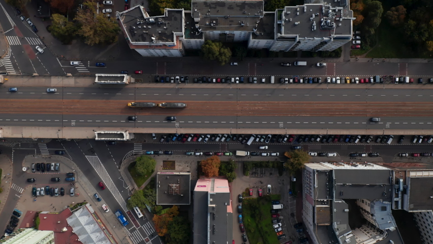 Aerial birds eye overhead top down panning view of transport in city. Tracking of tram running on tracks in middle of wide street. Warsaw, Poland