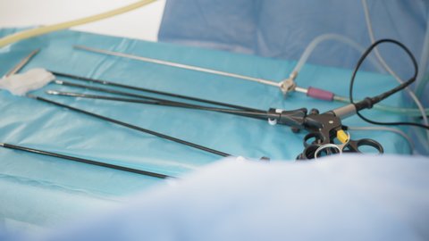 Laparoscopic scissors and graspers on blue desk. Multifunction Laparoscopic Instruments. Close up of female hands in sterile gloves holding trocar for laparoscopy procedure