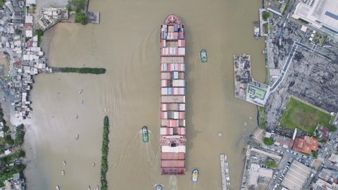 Aerial view of a large container freighter heads out to the sea assisted by tugs