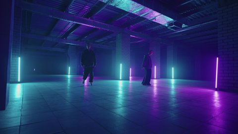 Two hip-hop dancers in neon light dance together in blue and purple colors.