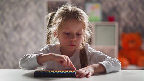 Thoughtful little kid with blonde plaits touches colorful abacus beads by finger during mental arithmetic lesson close view slow motion