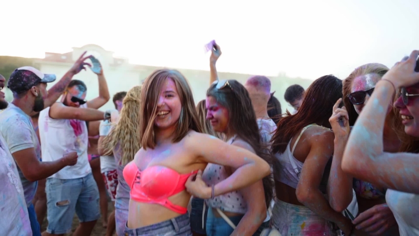 Jumping and dancing young people have fun and throw dry colors up in the air at Holi festival in slow motion. Friends celebrate hindu holiday and end of lockdown, covid pandemic, quarantine.
