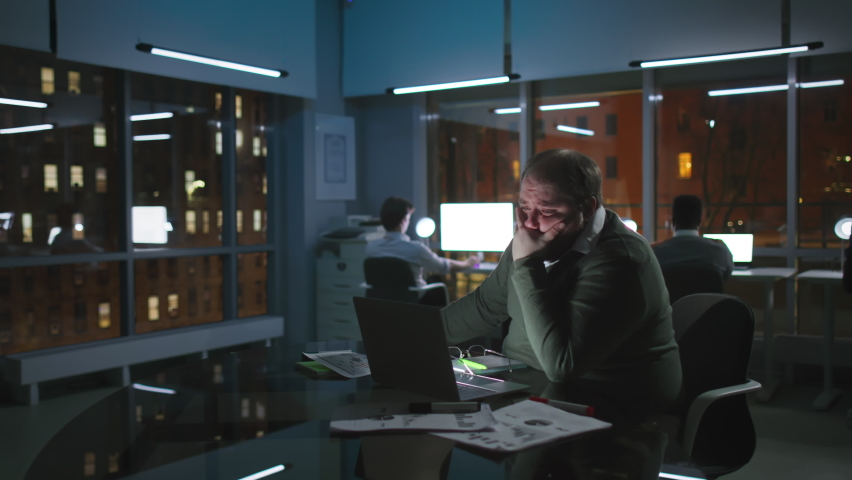 Tired and stressed fat entrepreneur cry working late in loft office with night old city view outside panoramic window.  | Shutterstock HD Video #1088812647