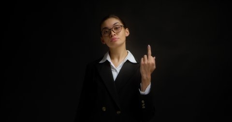 Confident, serious business woman in glasses and office clothes shows the middle finger, fuck you, fuck off, with a haughty face. Isolated on a black background in the studio