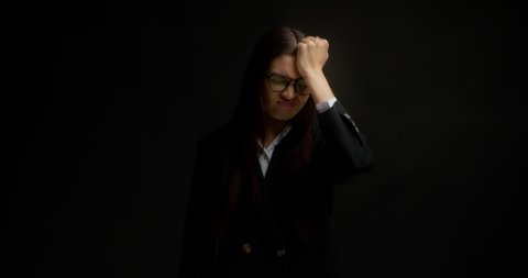 Business woman with long dark hair, glasses and office clothes forgot something, holds her forehead with her fist, bad memory. Isolated on a black background