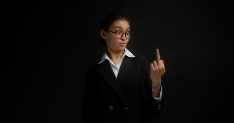 Guirky business woman in glasses and office clothes shows the middle finger, fuck you, fuck off, is surprised and smiles. Isolated on a black background in the studio
