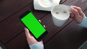 Womans hand use green screen smartphone for online shopping at cafe table with coffee cup