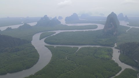 Fly left to right aerial view in area of NAI HGOP pier of Ao Phang - Nga in Thailand to mountain and show line of water with mangroves along the sides and cloudy sky