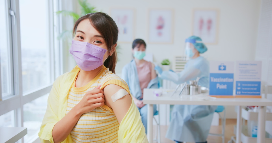 asian woman wearing face mask receiving coronavirus vaccine and she shows her arm to you with ok gesture in hospital Royalty-Free Stock Footage #1088815263