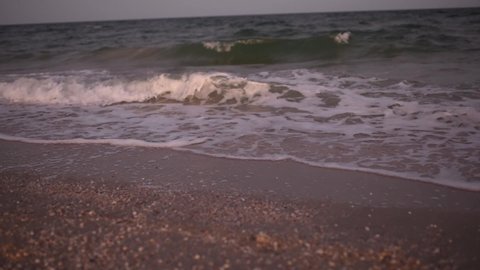 white flip-flops in seashells and sand on the shores of a stormy sea with waves After sunset. camera translates from beach shoes to the sea.