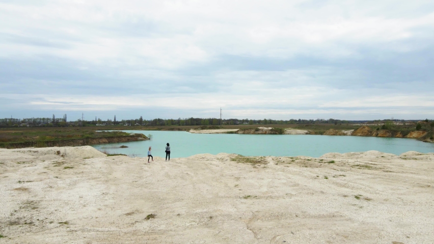 Drone flying low over travel family at lake shore, journey of mother, father daughter admire the view, happy family. Amazing industrial landscape, on Emerald lake in a flooded quarry, opencast mine
