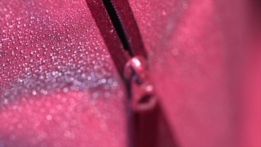 Macro focus shift shot of the zipper on the Gore-Tex membrane jacket does not allow moisture to pass through. Slow motion close-up of water drops on the pink waterproof clothing. Royalty-Free Stock Footage #1088822685