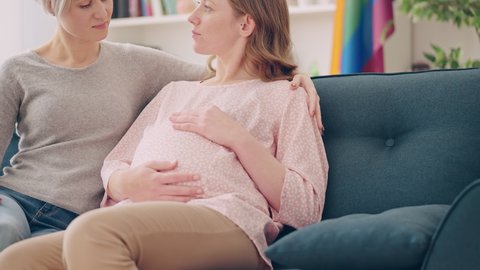 Two gay women expecting a baby, happy couple sitting and talking on couch