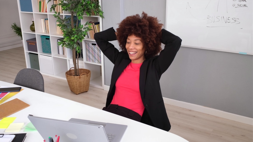 Smiling businesswoman sitting at desk with hands behing head
