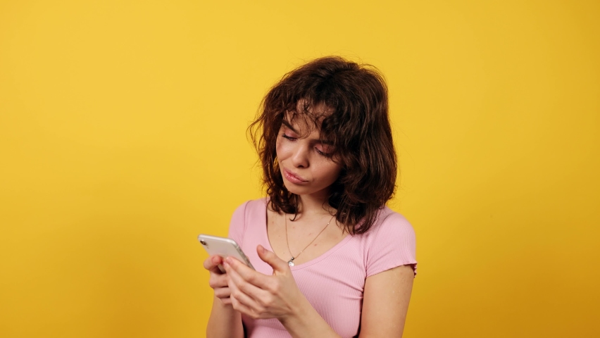 Bored woman scrolling on her phone on yellow background in studio. Phone addiction.  Royalty-Free Stock Footage #1088825249