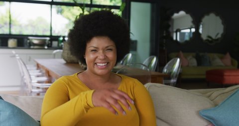 Video of happy plus size african american woman sitting on sofa. lifestyle, leisure, spending free time at home.