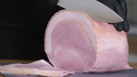 Prosciutto cotto with lard. Slicing traditional ham into pieces on cutting board with a knife. Thin slices of meat. Concept of delicious food snacks and cooking. Man with knife is cutting slim slices 